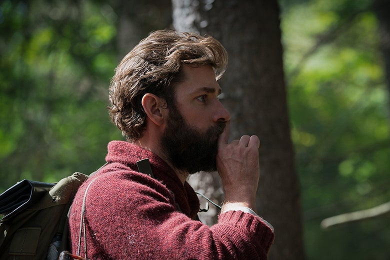 John Krasinski shushes someone in profile. The shot is him from the chest up.